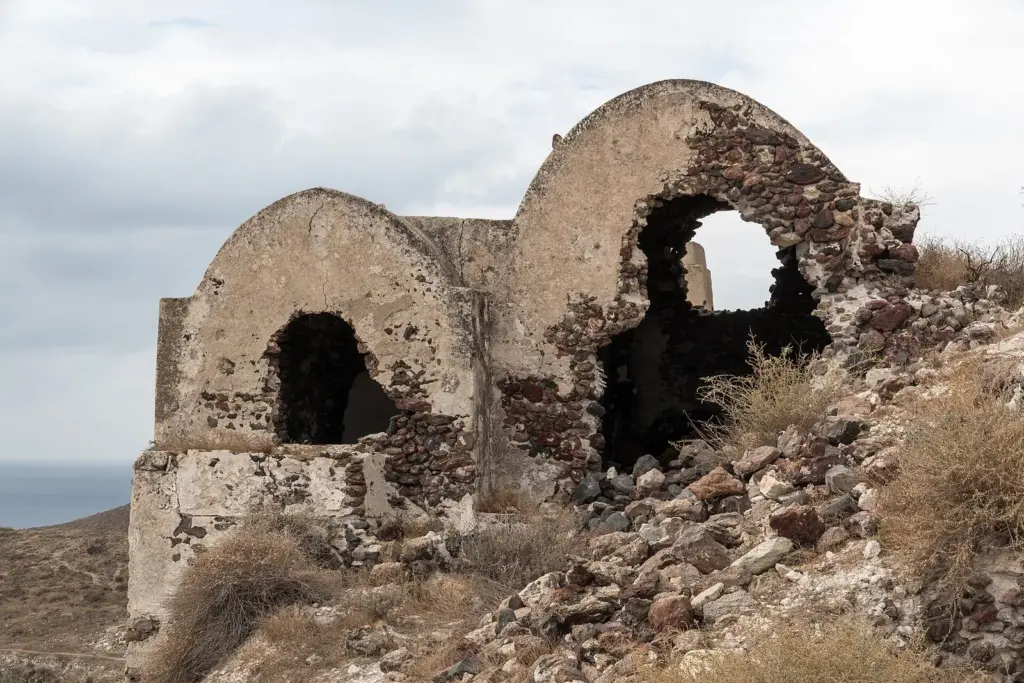 Weathered stone ruins with arched openings on the hillside of Akrotiri village