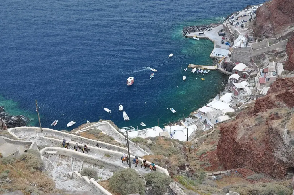 Ammoudi harbor far below Oia, with small boats, tavernas and the zigzag steps down the red cliffs