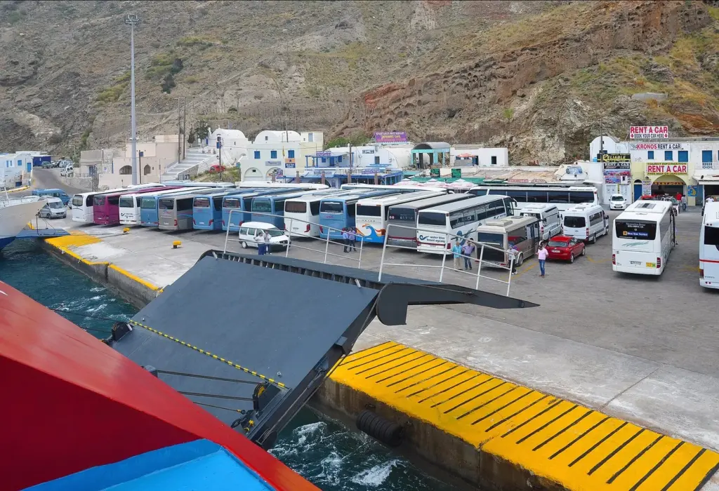 Tour buses and rental cars lined up on the quay at Athinios port as a ferry ramp comes down
