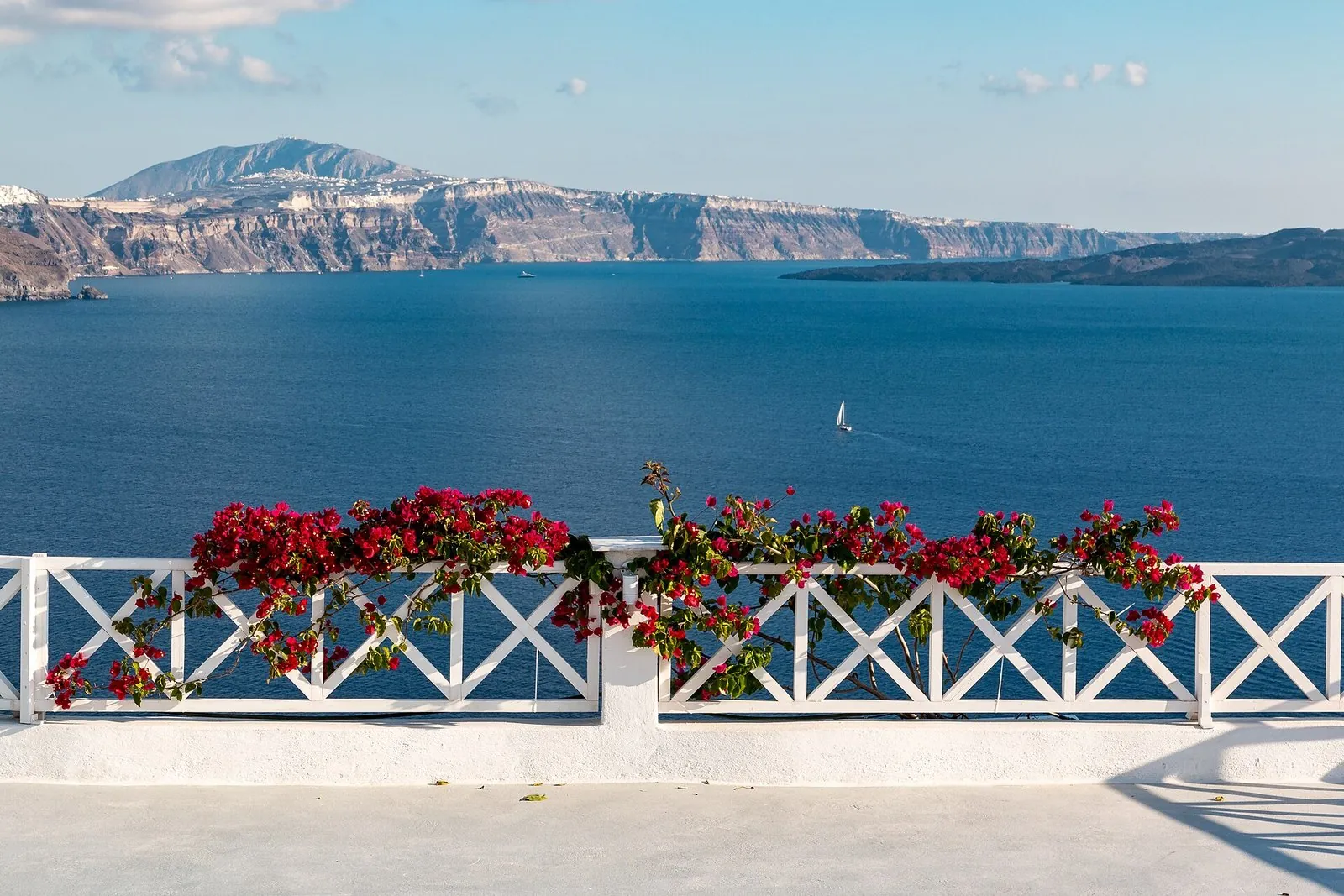 Best time to visit Santorini: red bougainvillea on a white terrace railing above the blue caldera in late September