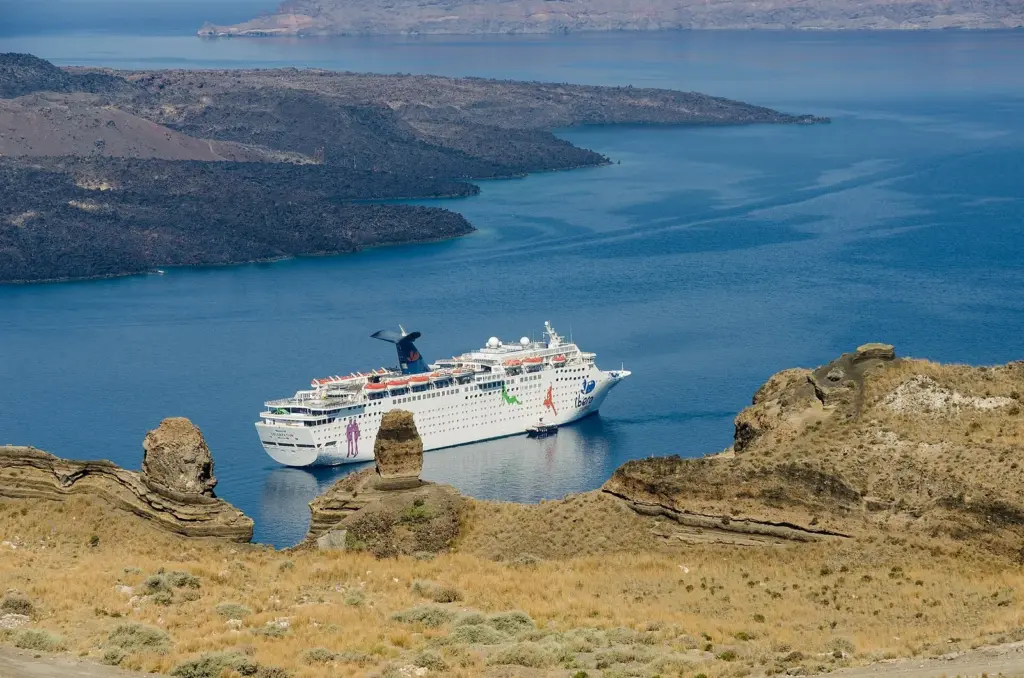 A white cruise ship anchored in the Santorini caldera beside volcanic rocks