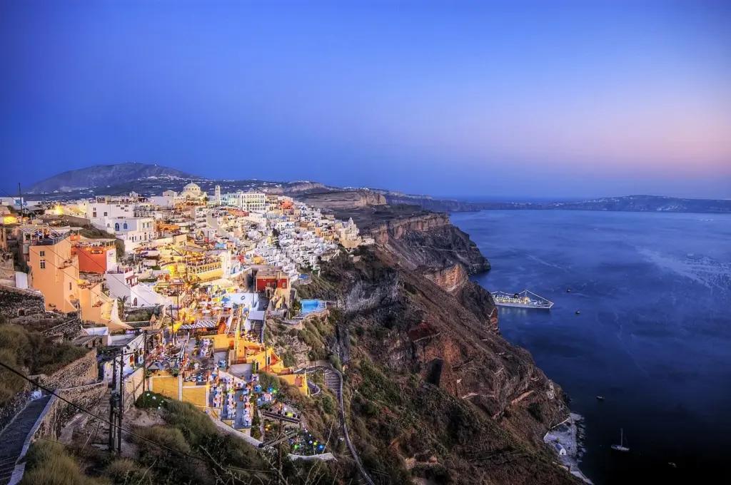 Fira's cliffside buildings glowing in the evening light above the caldera in late August