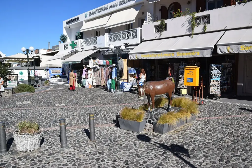 A paved square in Fira with souvenir shops, a yellow mailbox and a donkey statue