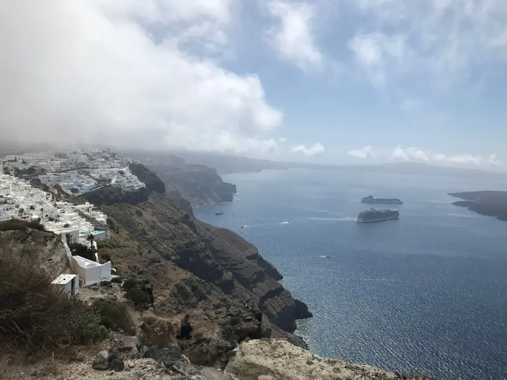 Firostefani and Fira on the caldera rim above the sea, with a cruise ship below and low clouds