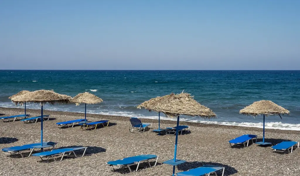Sunbeds and straw umbrellas on the dark pebble beach at Kamari