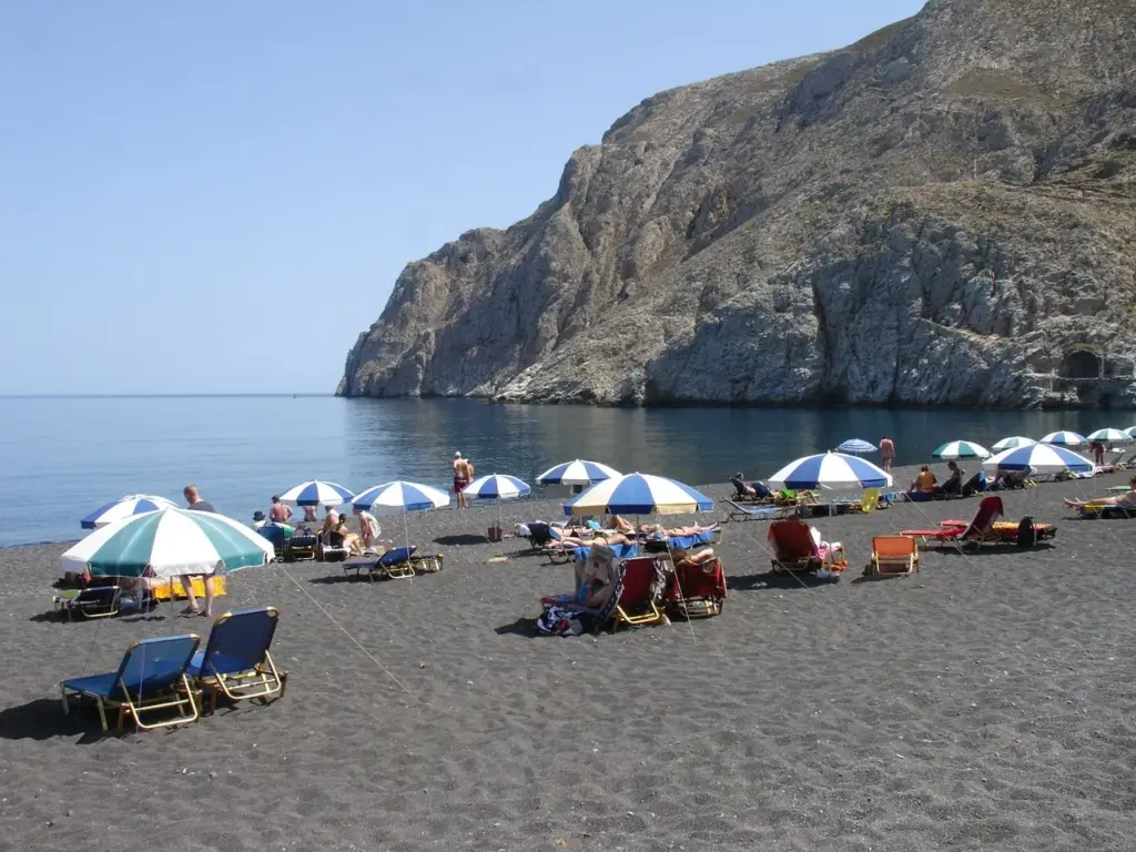 Beach umbrellas and sunbeds on Kamari's black beach below the Mesa Vouno cliffs