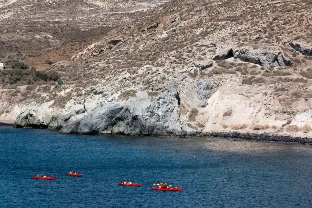 Kayakers paddling in the calm bay near Red Beach below pale volcanic cliffs