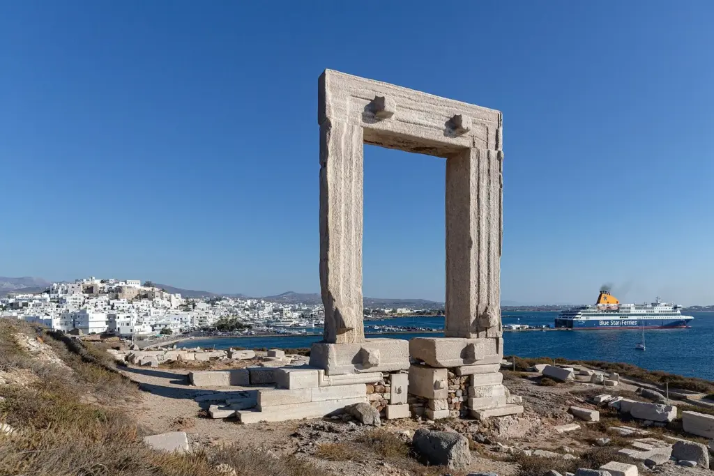 The Portara marble gateway on Naxos framing the town, with a Blue Star ferry in the harbor