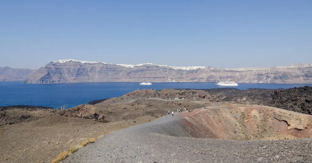 Visitors hiking a gravel path across dark lava fields on Nea Kameni, with the caldera cliffs behind
