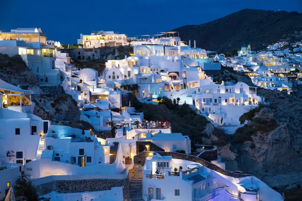 Oia at dusk, its white houses and hotel terraces lit up along the dark caldera cliff