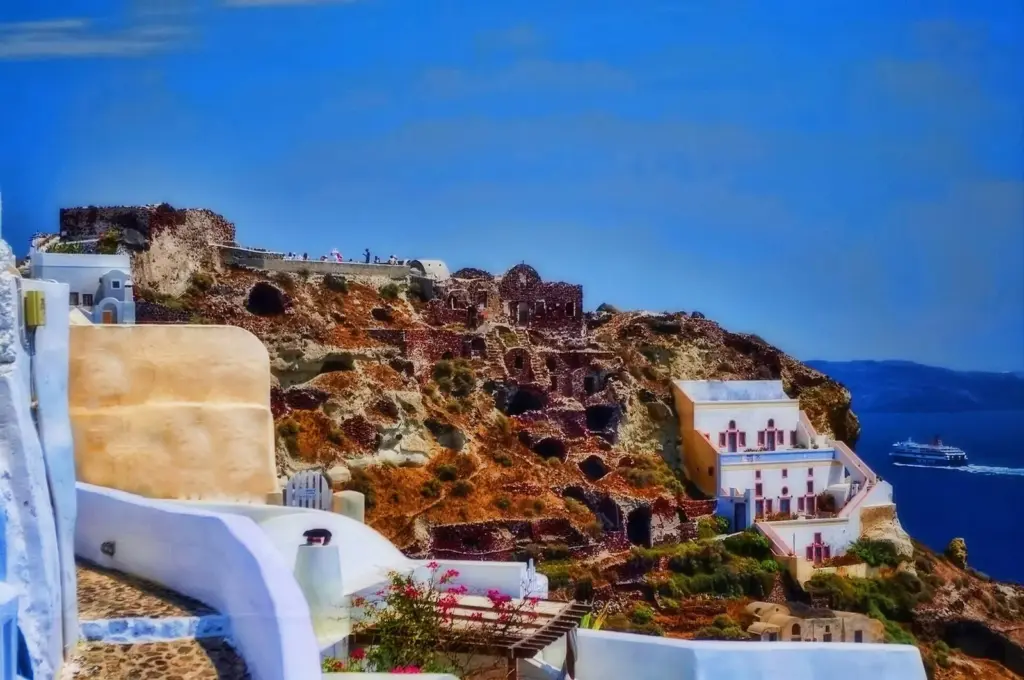 Visitors gathered on the ruined stone walls of Oia's castle above the caldera, with houses stepping down the cliff
