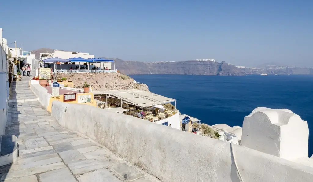 Oia's marble-paved main path running along whitewashed walls above the caldera, with restaurant terraces below