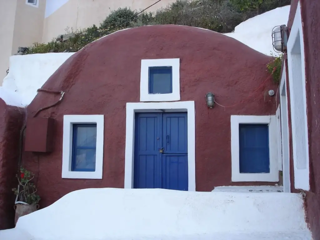 The vaulted red facade of a traditional cave house with blue doors in Oia