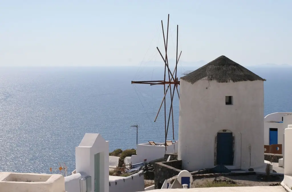 A whitewashed windmill with a thatched roof and bare sails above the sea at Oia