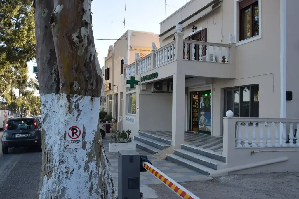 A pharmacy with a green cross sign on the road between Fira and Karterados