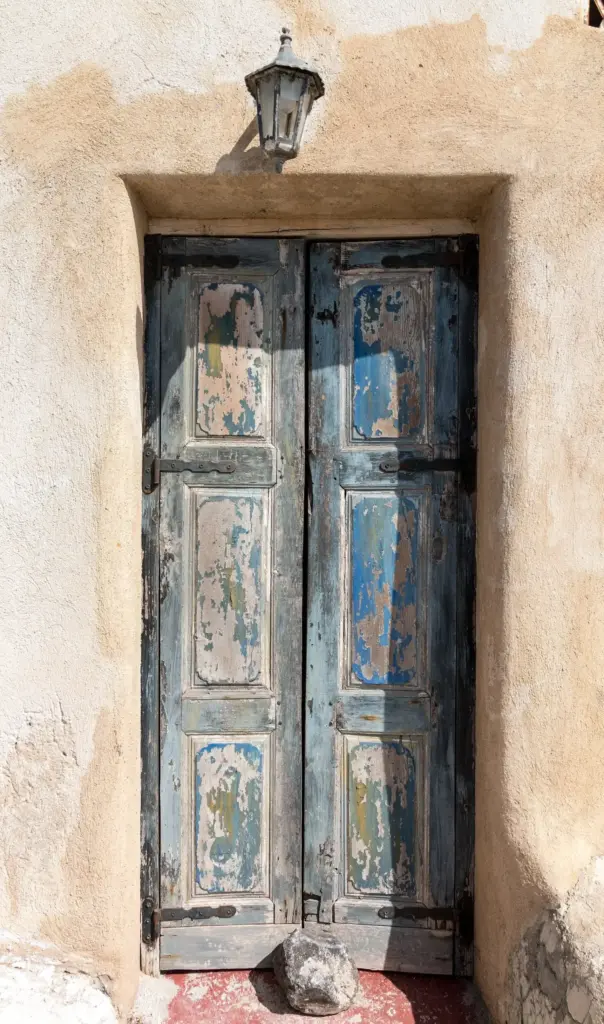 A weathered blue wooden door set in a pale stone wall in the village of Pyrgos