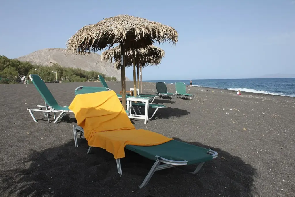 An empty black-sand beach with thatched umbrellas and sunbeds under a clear sky in mid-April