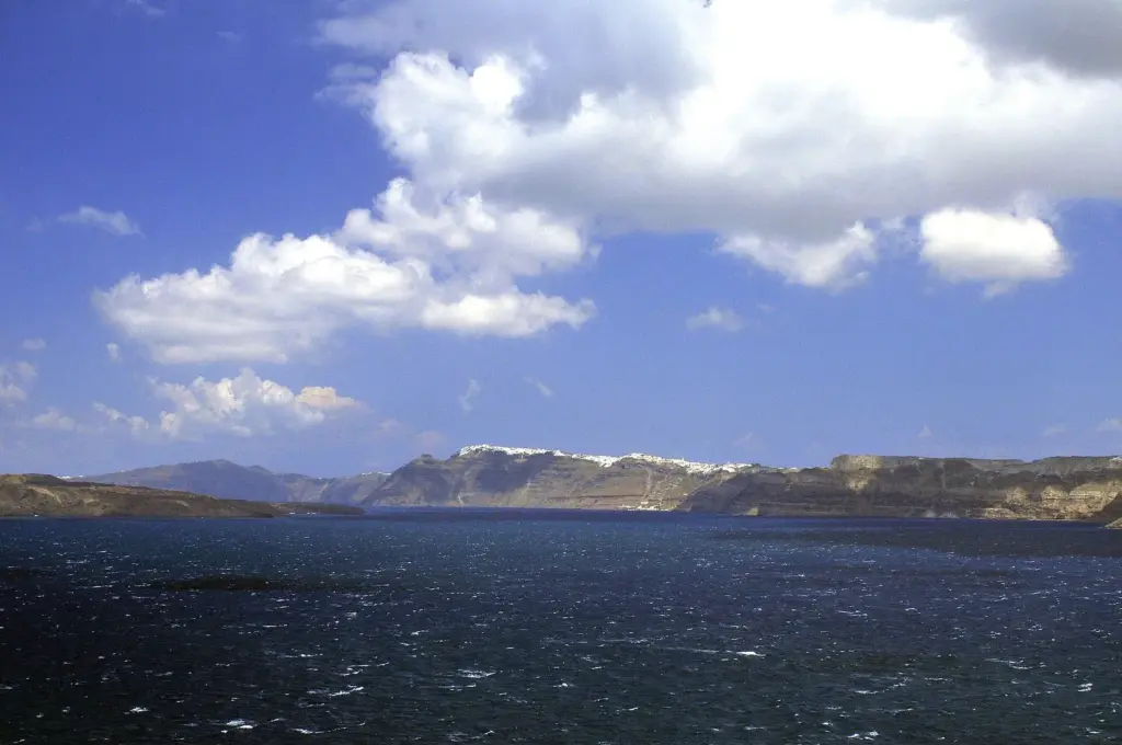 White clouds over the blue caldera with Fira on the rim, seen from Akrotiri in mid-April