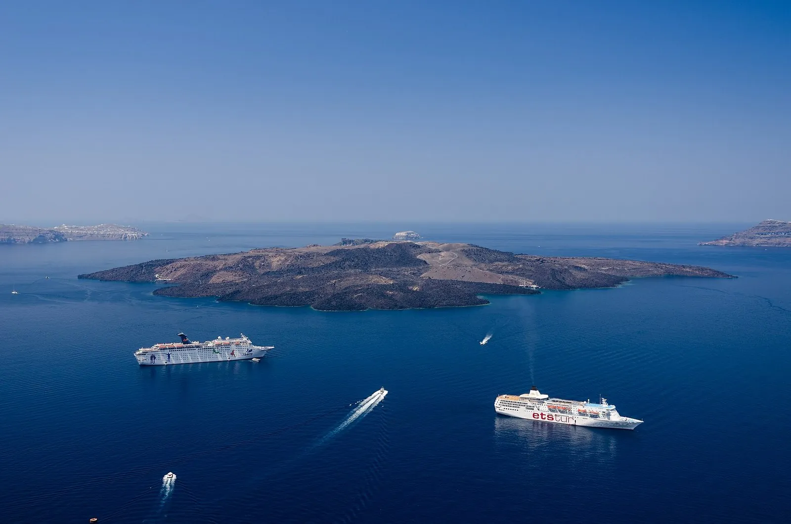 Santorini travel guide: the caldera seen from Fira, with the dark volcanic island of Nea Kameni and cruise ships at anchor