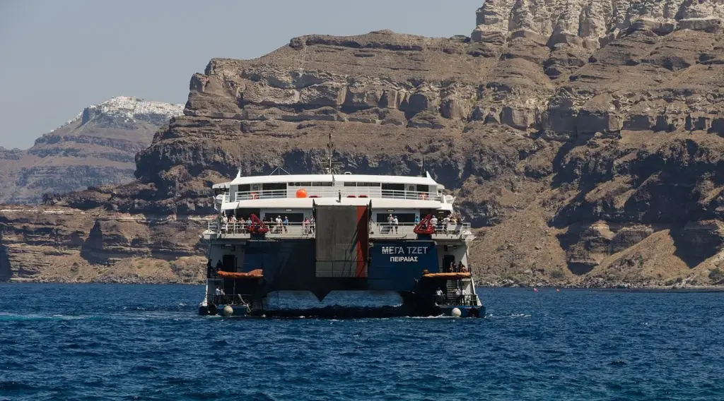 A high-speed catamaran ferry arriving at Athinios harbor beneath Santorini's caldera cliffs