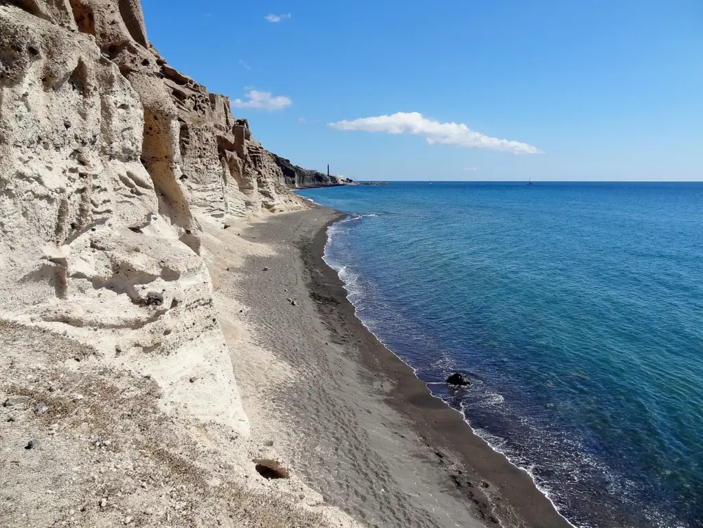 Pale wind-carved cliffs above the dark sand and blue water of Vlychada beach
