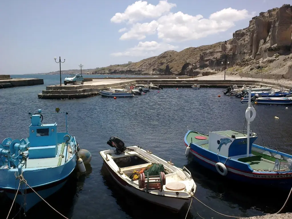 Small painted fishing boats moored in the little harbor at Vourvoulos under layered volcanic cliffs