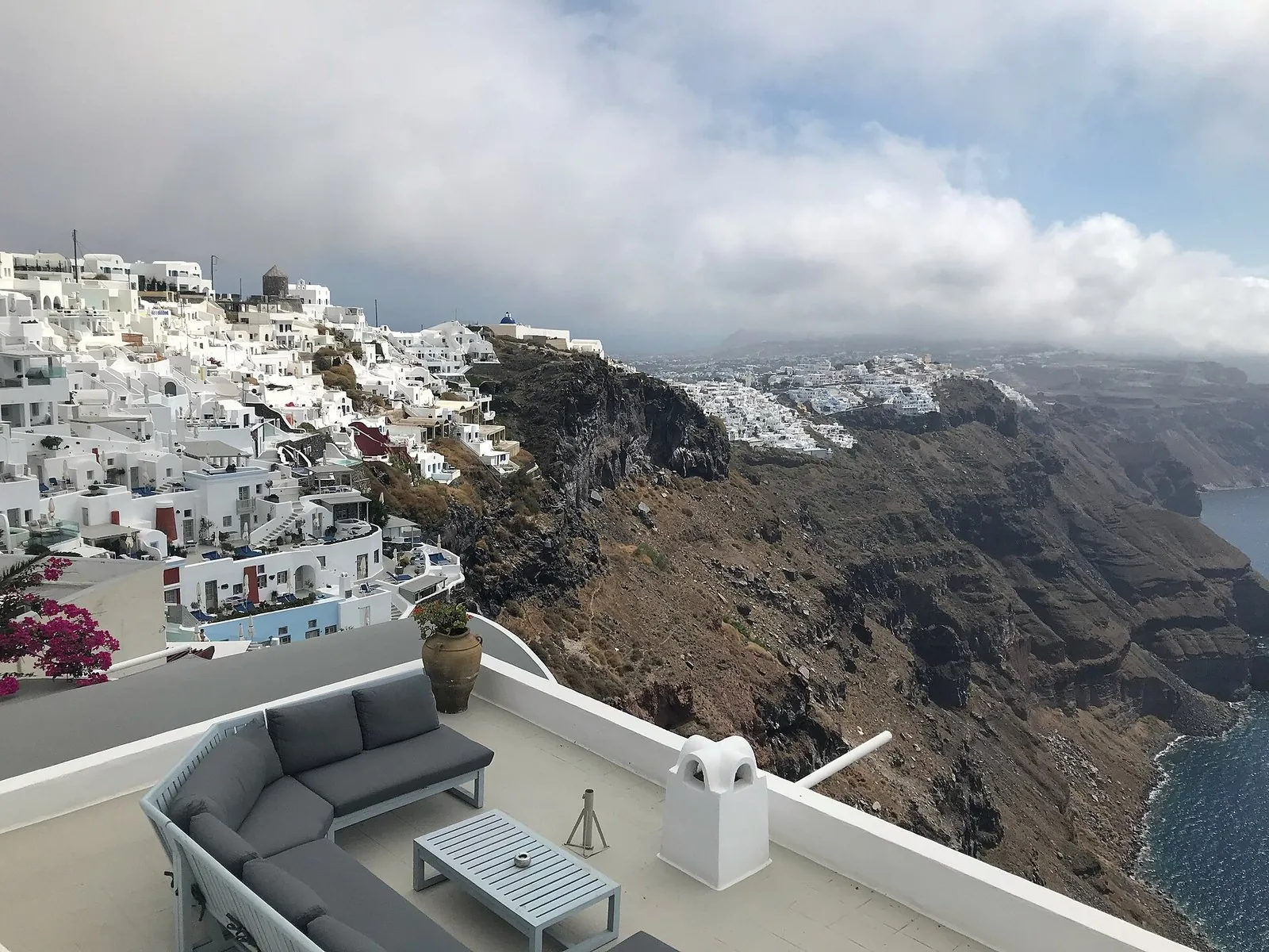 Where to stay in Santorini: a hotel terrace above the caldera looking toward Firostefani and Fira along the cliff rim