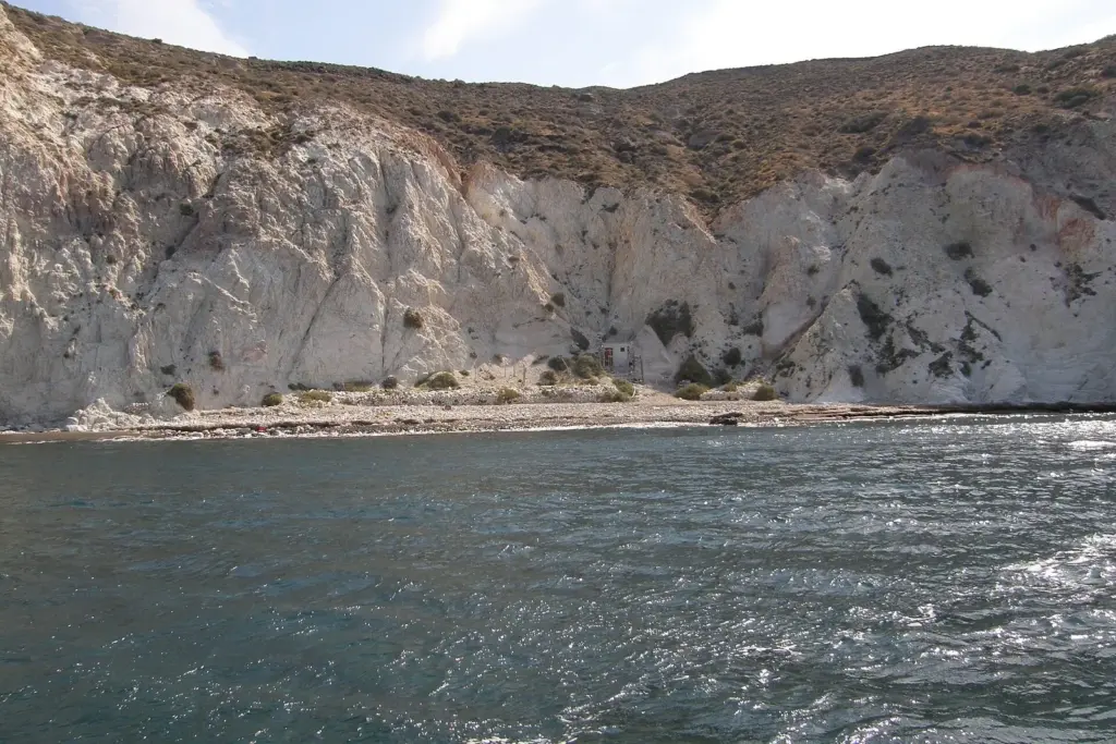White volcanic cliffs above a narrow dark beach seen from a boat off White Beach