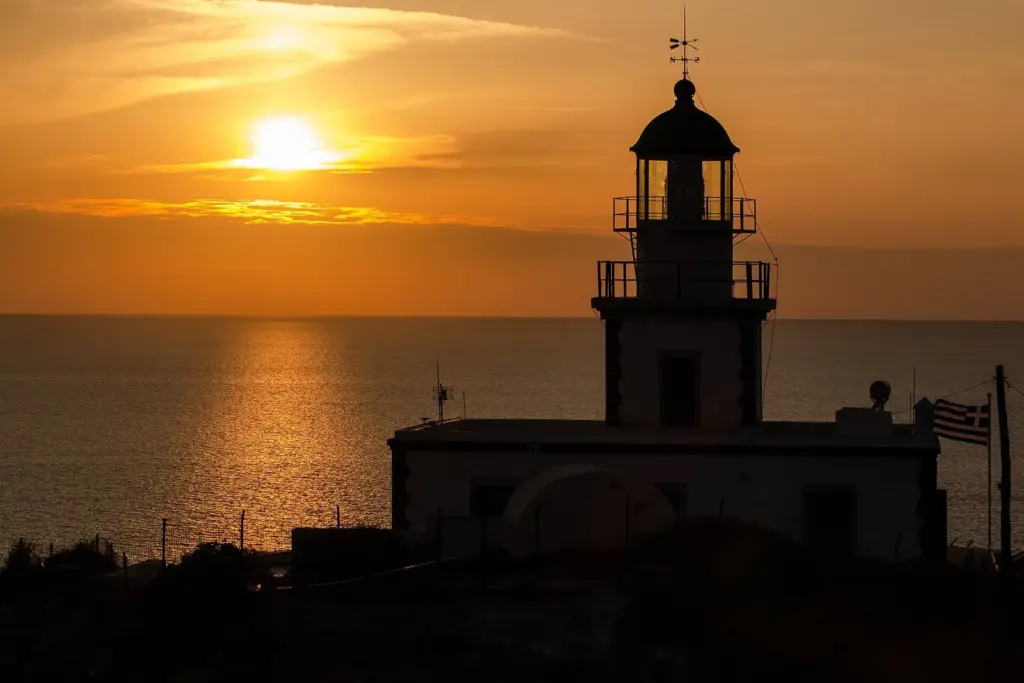The Akrotiri lighthouse silhouetted against an orange sunset over the sea