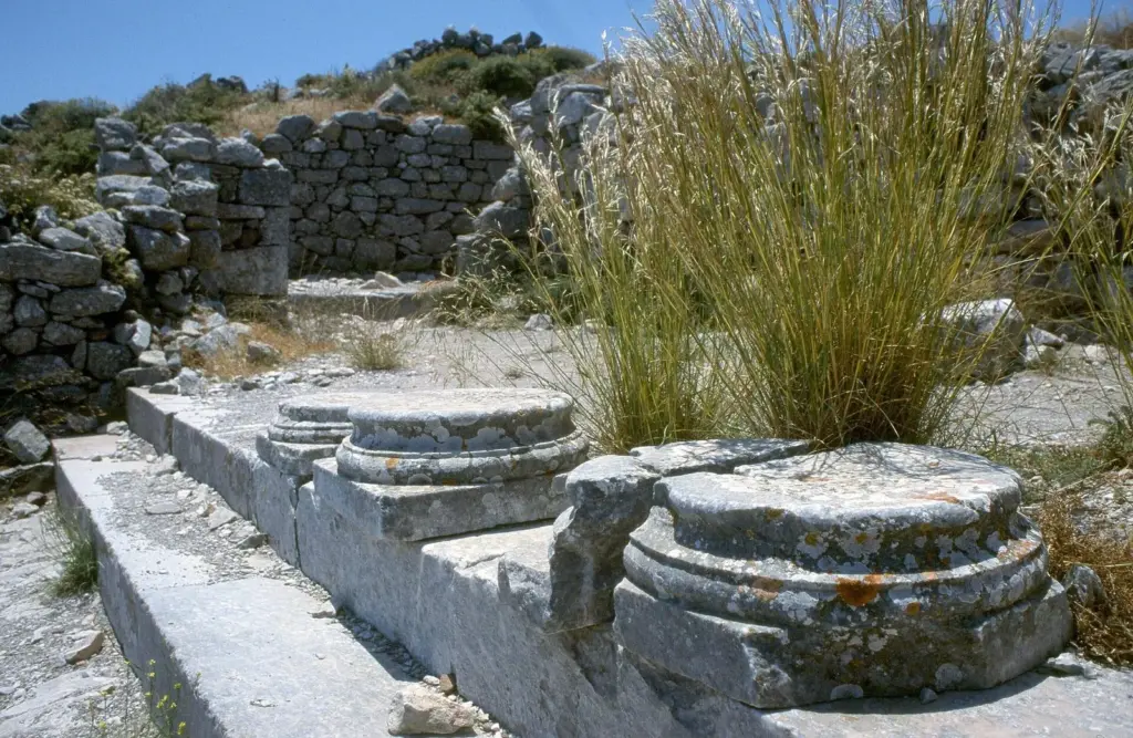 Weathered marble column bases from a portico among rough stone walls and tufts of grass on a ridge