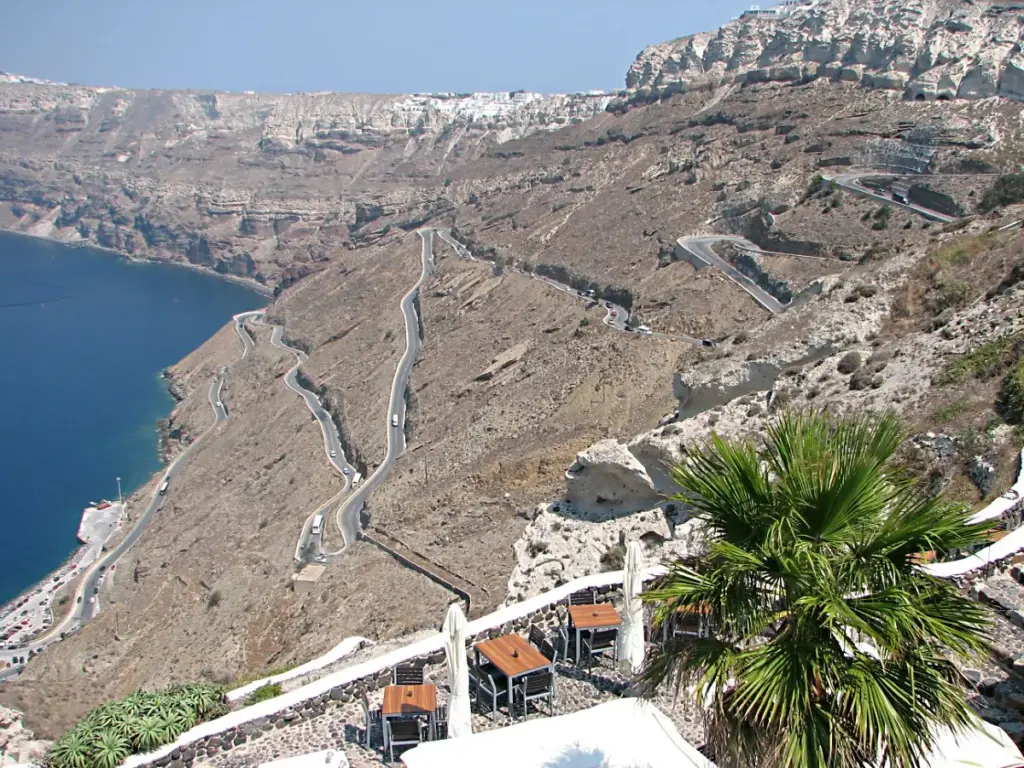 Switchback road zigzagging down a steep brown cliff to the ferry port beside the caldera