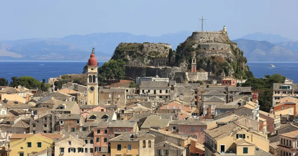 Tiled roofs and a bell tower of Corfu's old town below the hill of the Old Fortress, with mountains across the sea