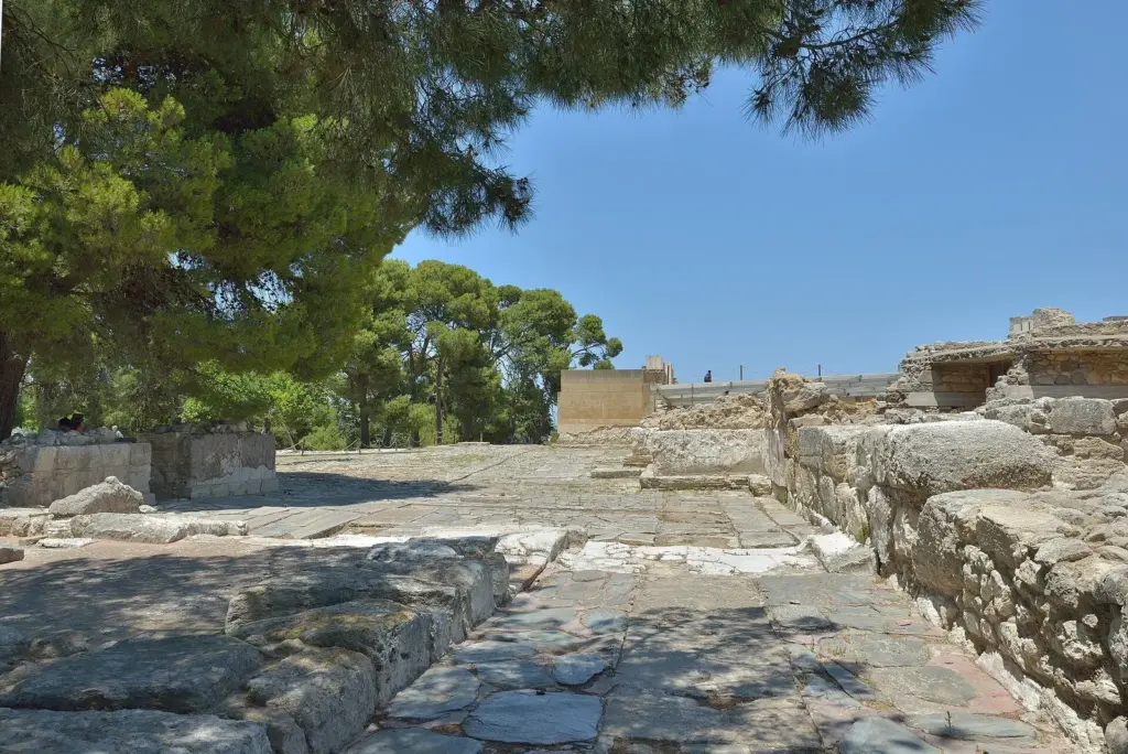 Stone paving and low walls of the west court at the Minoan palace of Knossos, framed by pine trees