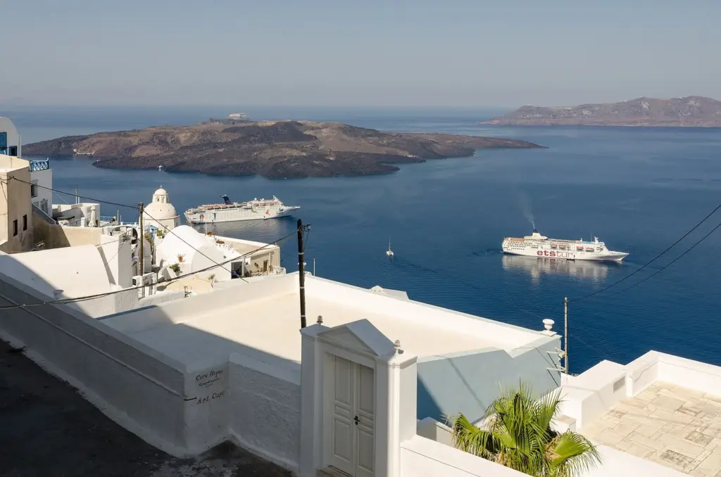 A whitewashed alley on the caldera edge in Fira looking across to Nea Kameni, with cruise ships at anchor