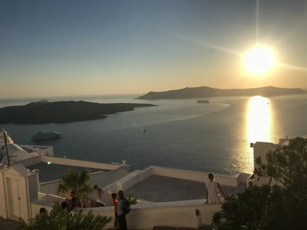 The sun low over the caldera, glittering on the water beyond Nea Kameni, seen from a terrace in Fira