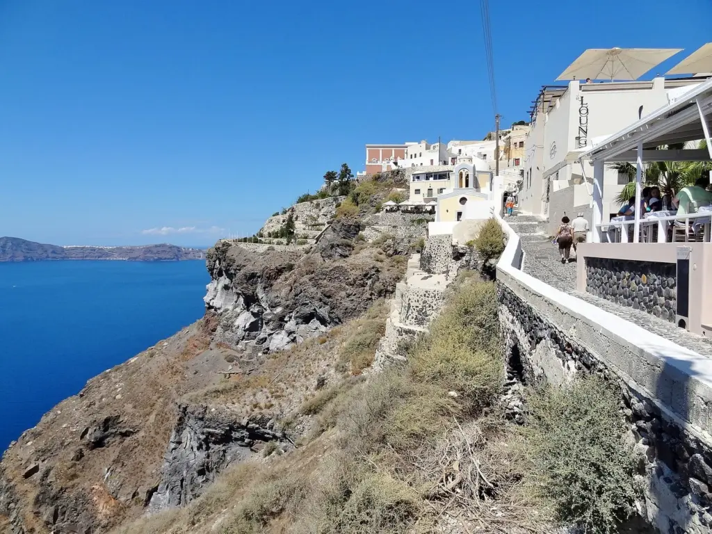 Caldera-edge walkway in Fira lined with whitewashed buildings and cafe terraces above the deep blue sea