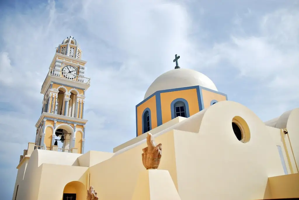 Pale yellow Catholic cathedral with a tall clock tower and a blue-trimmed dome against a cloudy sky