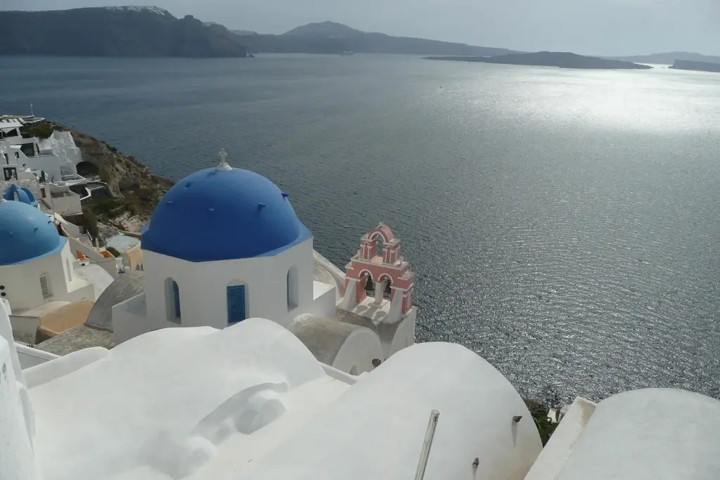 Blue-domed church and white rooftops beside the caldera path, with the sea glittering below