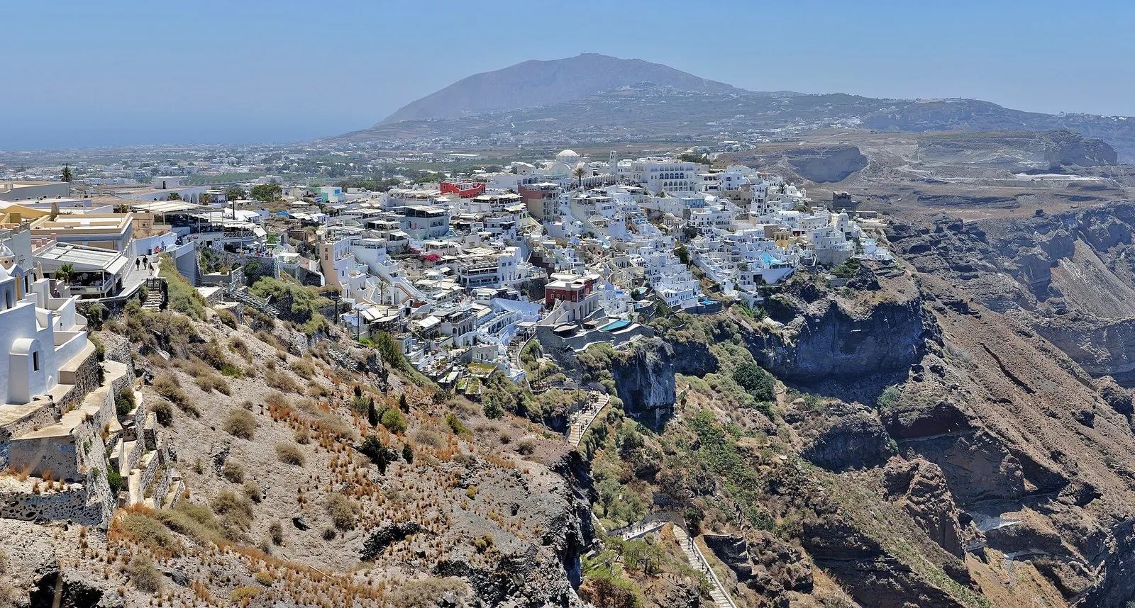 Fira Santorini spread along the caldera cliff top, with whitewashed buildings, the steep slope and Profitis Ilias mountain beyond