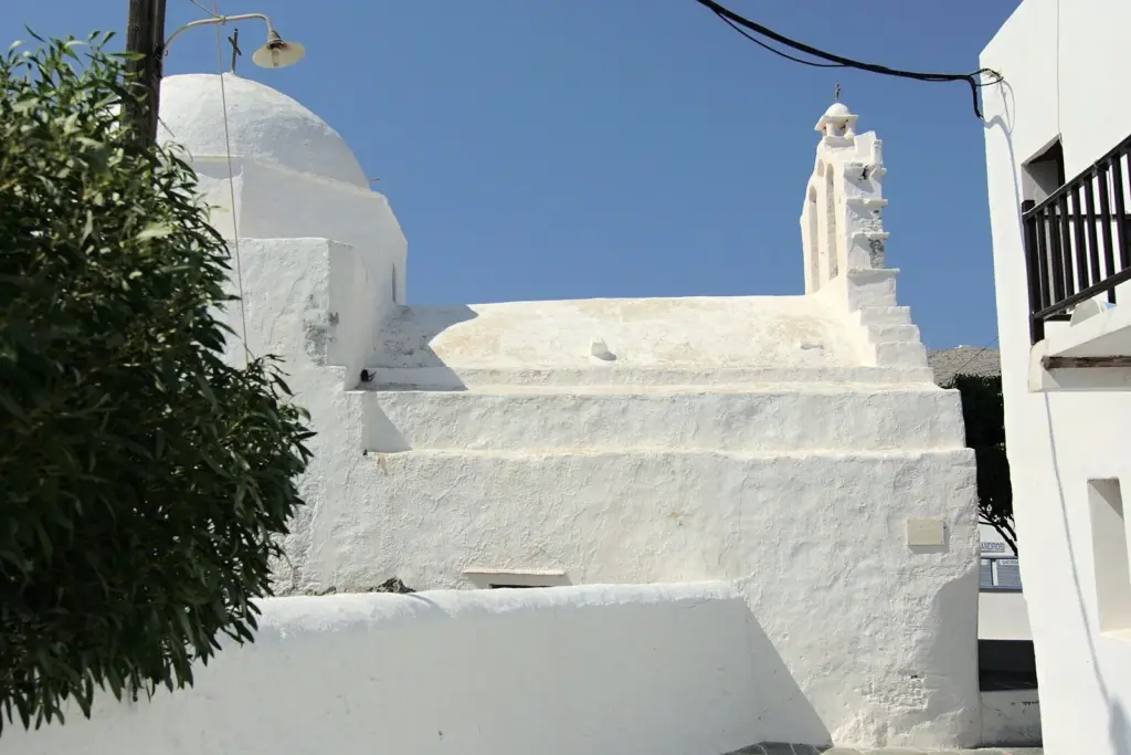 A brilliant white church with a bell gable and a curved roofline against a blue sky in the Chora of Folegandros