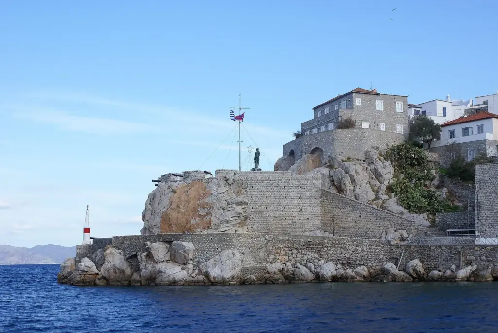 Stone mansions and a harbor wall with cannons on a rocky point at the entrance to Hydra's harbor