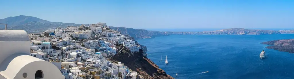 Panorama of Imerovigli's white houses on the caldera rim, with the cliffs curving away toward Oia and boats on the water