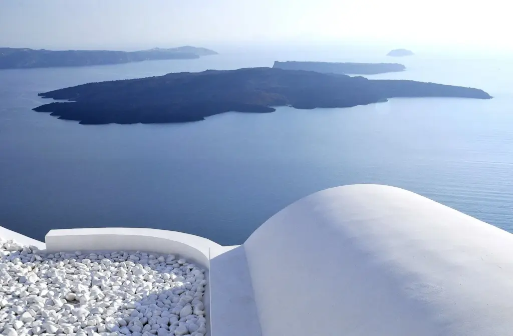 White rooftop terrace with chimneys in Imerovigli looking across the calm caldera to Nea Kameni