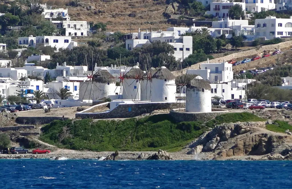 Whitewashed houses and a row of traditional windmills on a hillside above the sea on Mykonos
