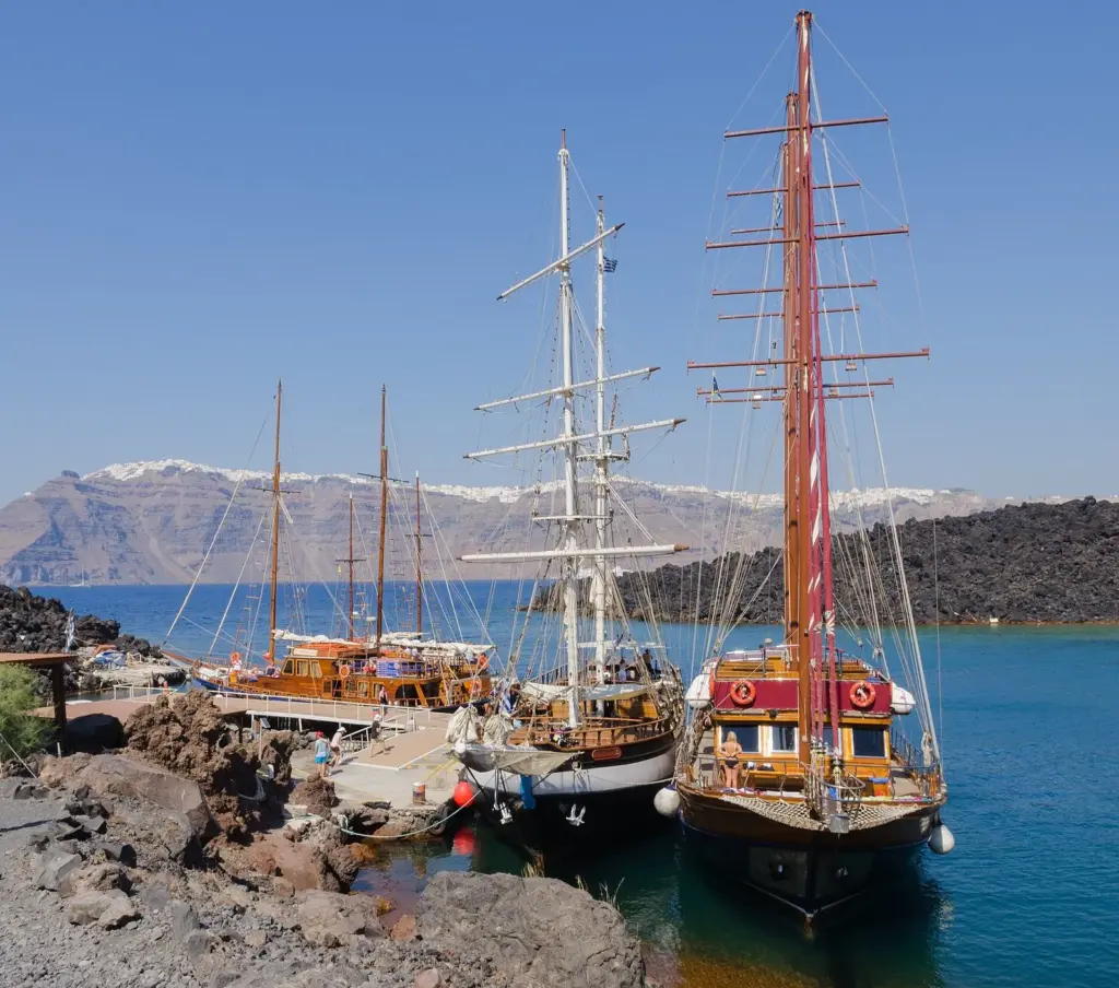Wooden tour boats with tall masts moored at a rocky landing on a dark volcanic island