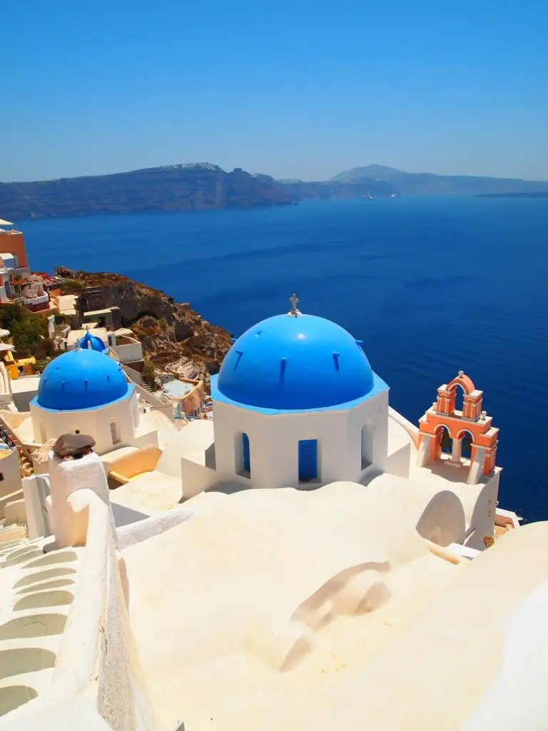 Blue-domed churches and a pink bell tower above the deep blue caldera in Oia