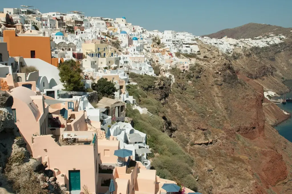 Oia's white and pastel houses stepping down the slope above the caldera, seen from the castle