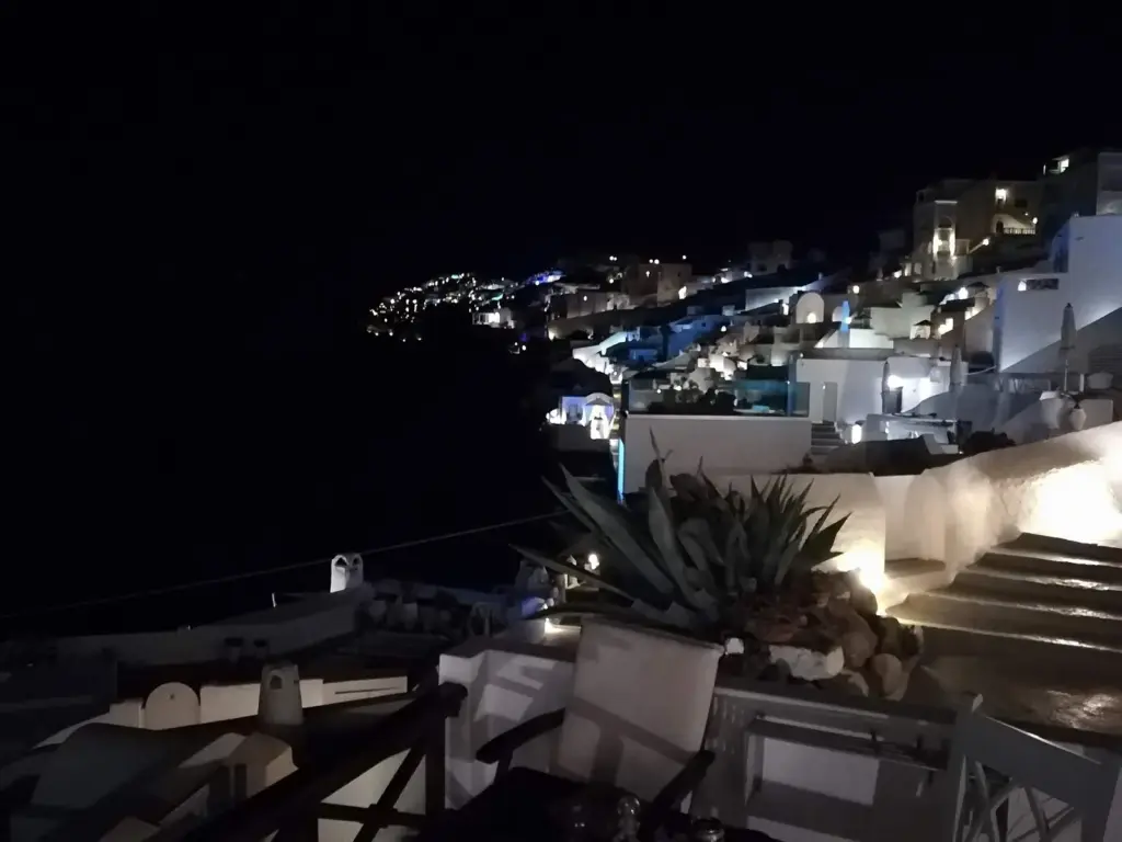 Oia's white houses and terraces lit up at night along the dark caldera