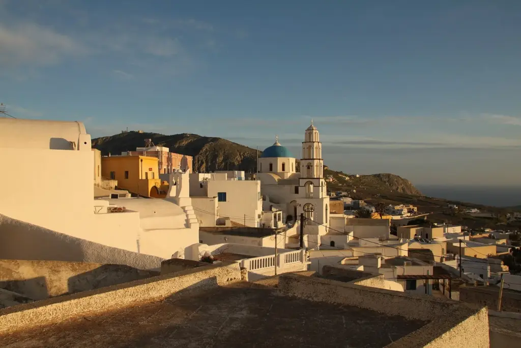 The whitewashed houses and bell towers of Pyrgos glowing in late-afternoon sun, with hills behind