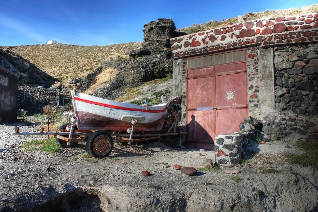 A red and white wooden fishing boat on a trailer in front of a red-doored stone boathouse